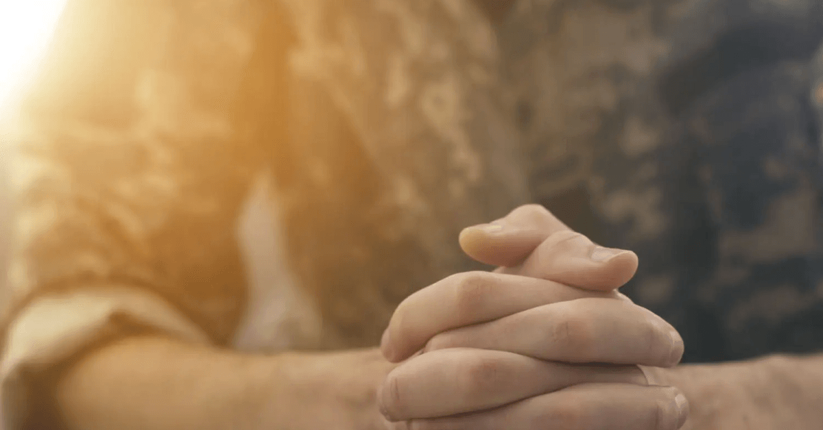 Hands of a veteran in military uniform, clasped together in reflection.